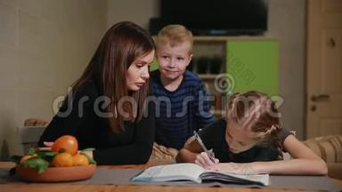 母女俩在做学校作业，一个小男孩在看。 哥哥帮忙做作业。